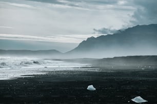 a black and white photo of a beach with mountains in the background