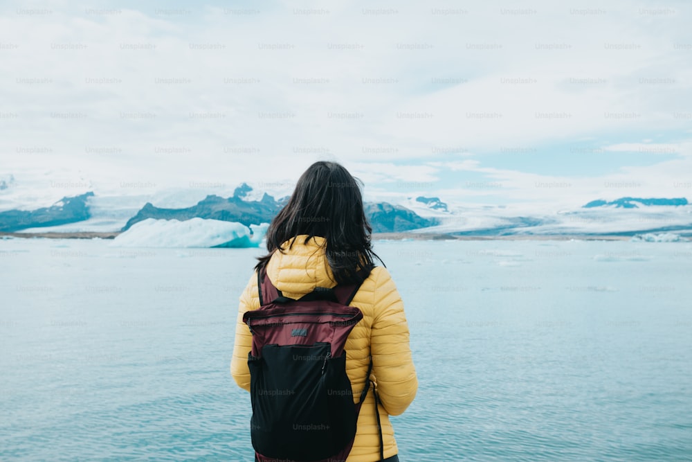 uma mulher com uma mochila olhando para fora sobre um corpo de água