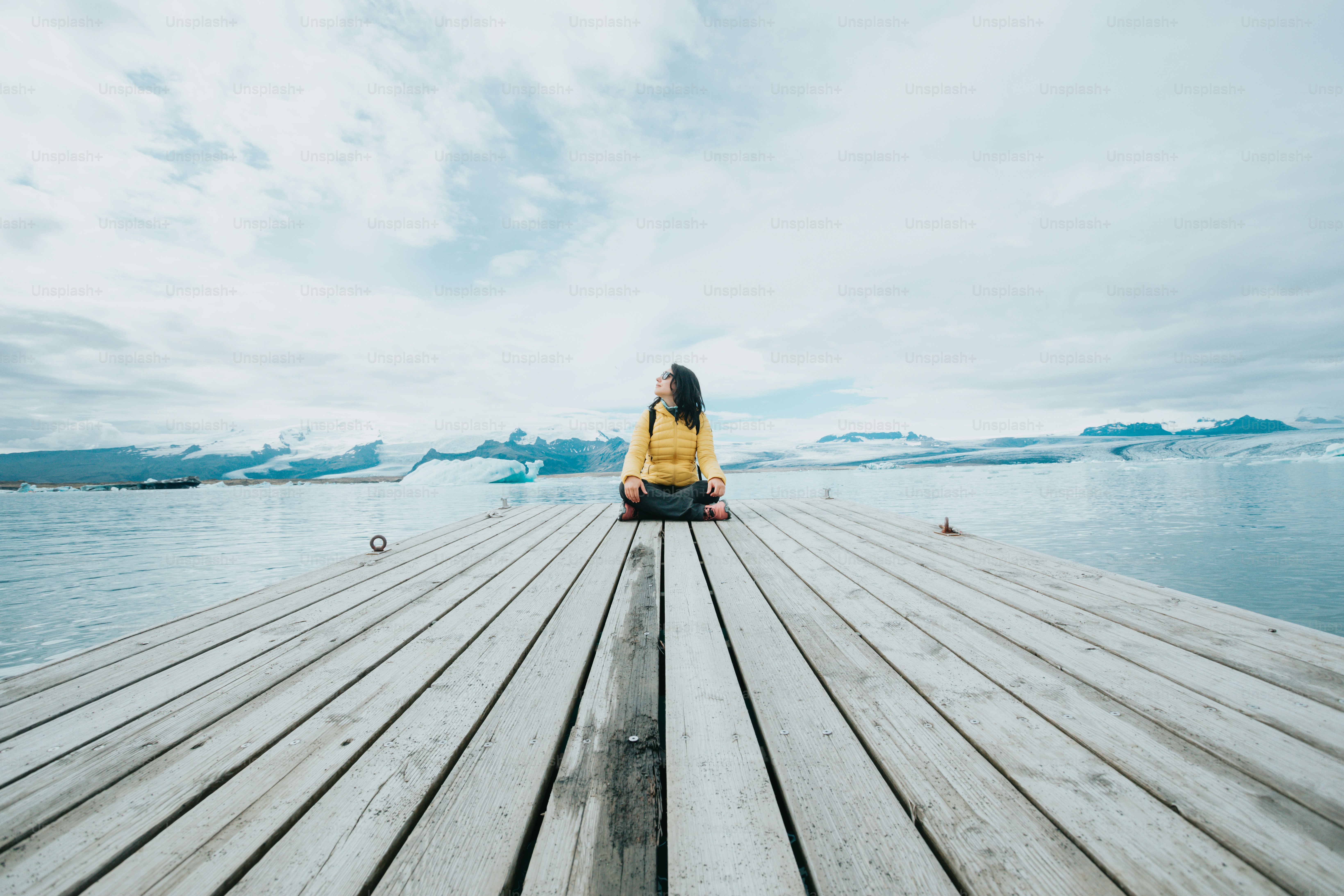 a woman is sitting on a dock by the water