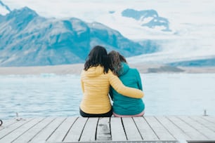 Due donne sedute su un molo che guardano un ghiacciaio