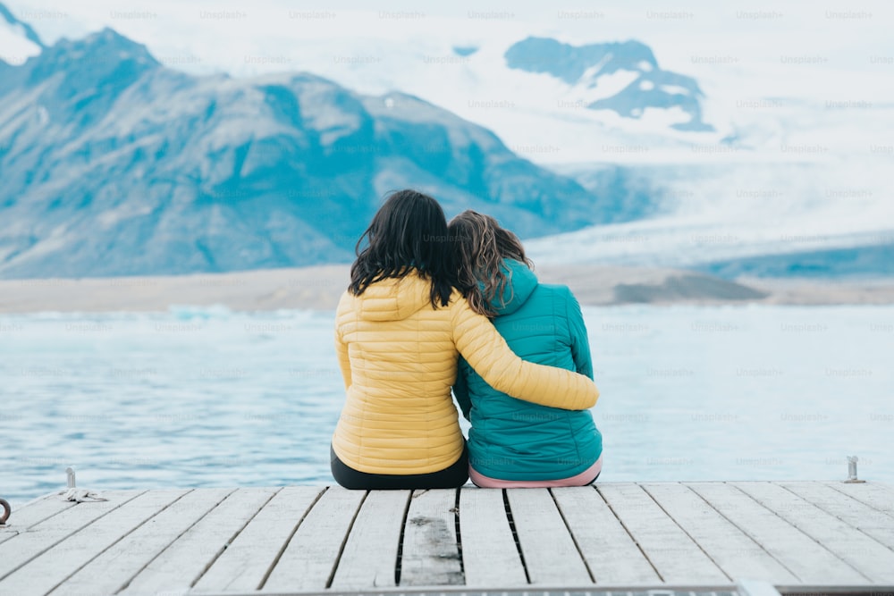 two women sitting on a dock looking at a glacier