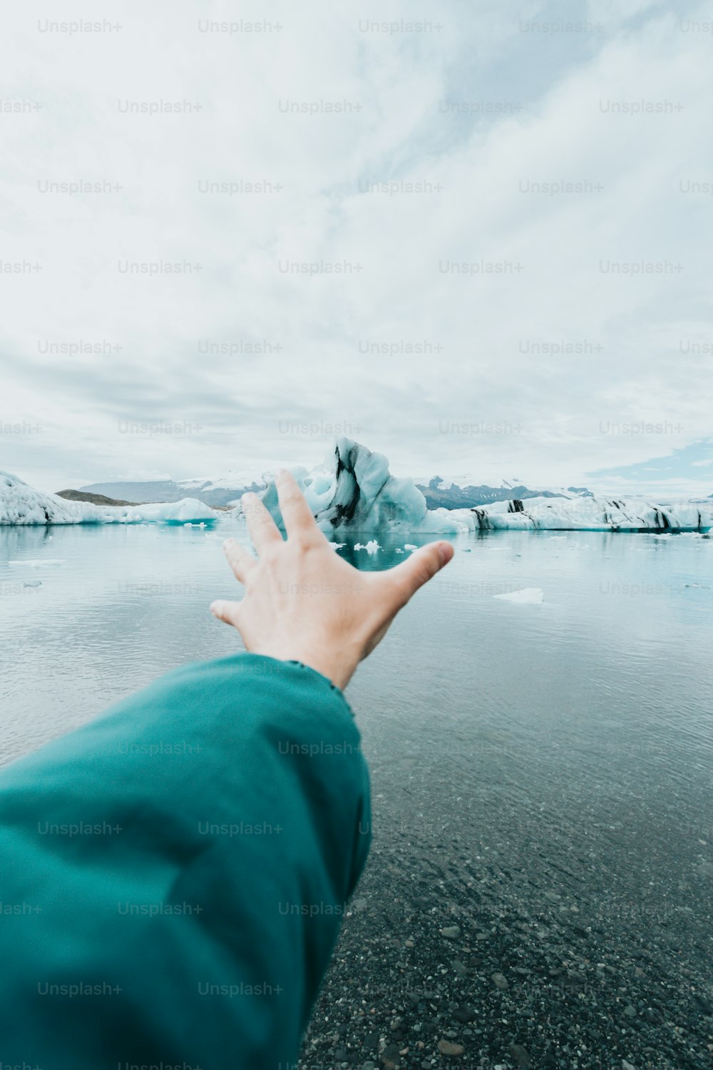 a person's hand reaching for an iceberg in the water
