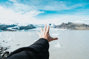 a hand reaching out towards a glacier lake