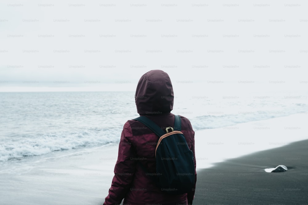 eine Person mit einem Rucksack, die am Strand spazieren geht