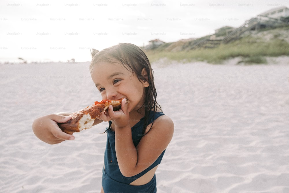 a little girl eating a slice of pizza on the beach