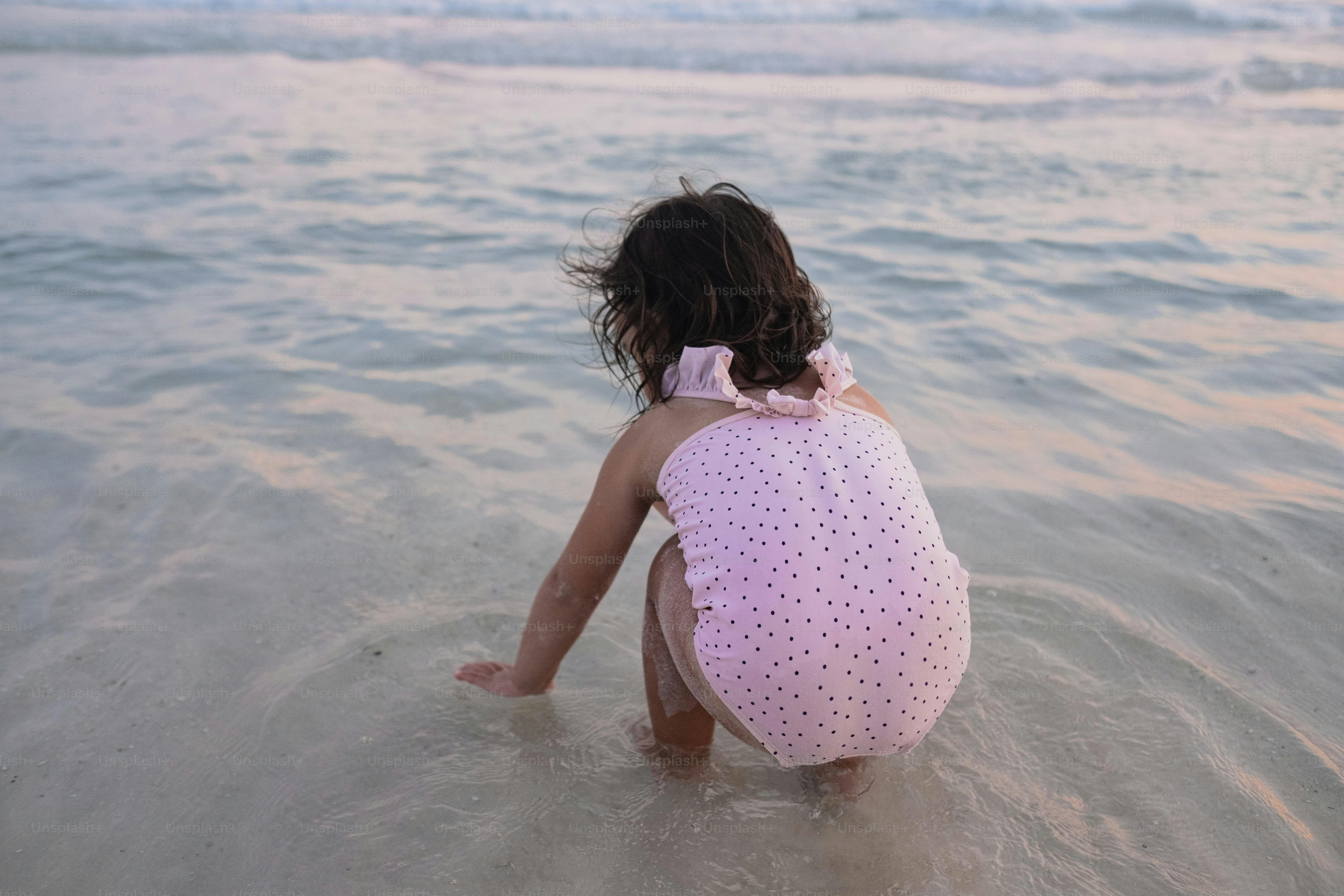 a little girl sitting in the water at the beach