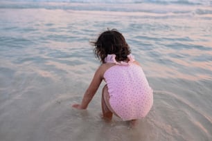 Ein kleines Mädchen, das im Wasser am Strand sitzt