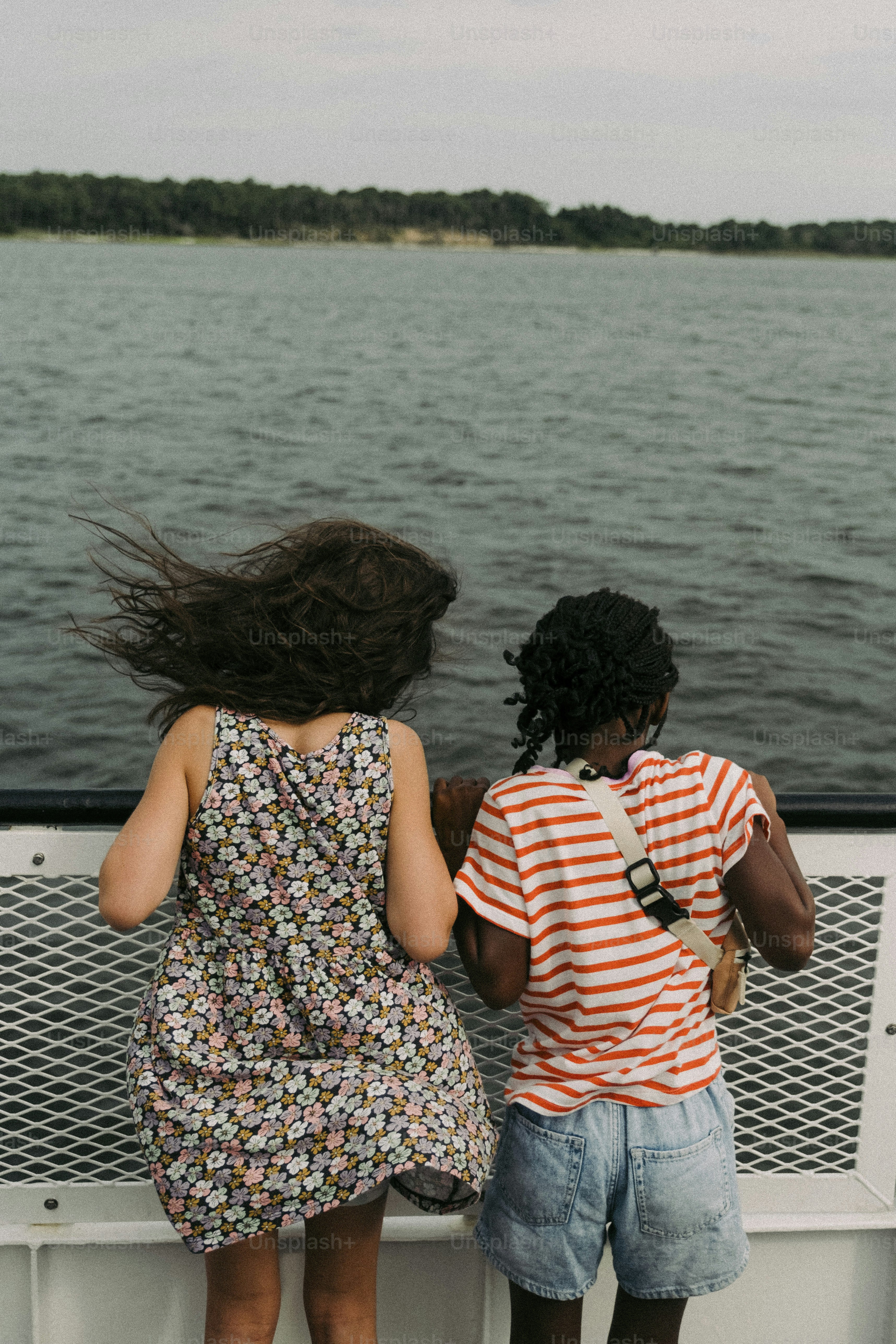 two young girls standing on a boat looking out at the water