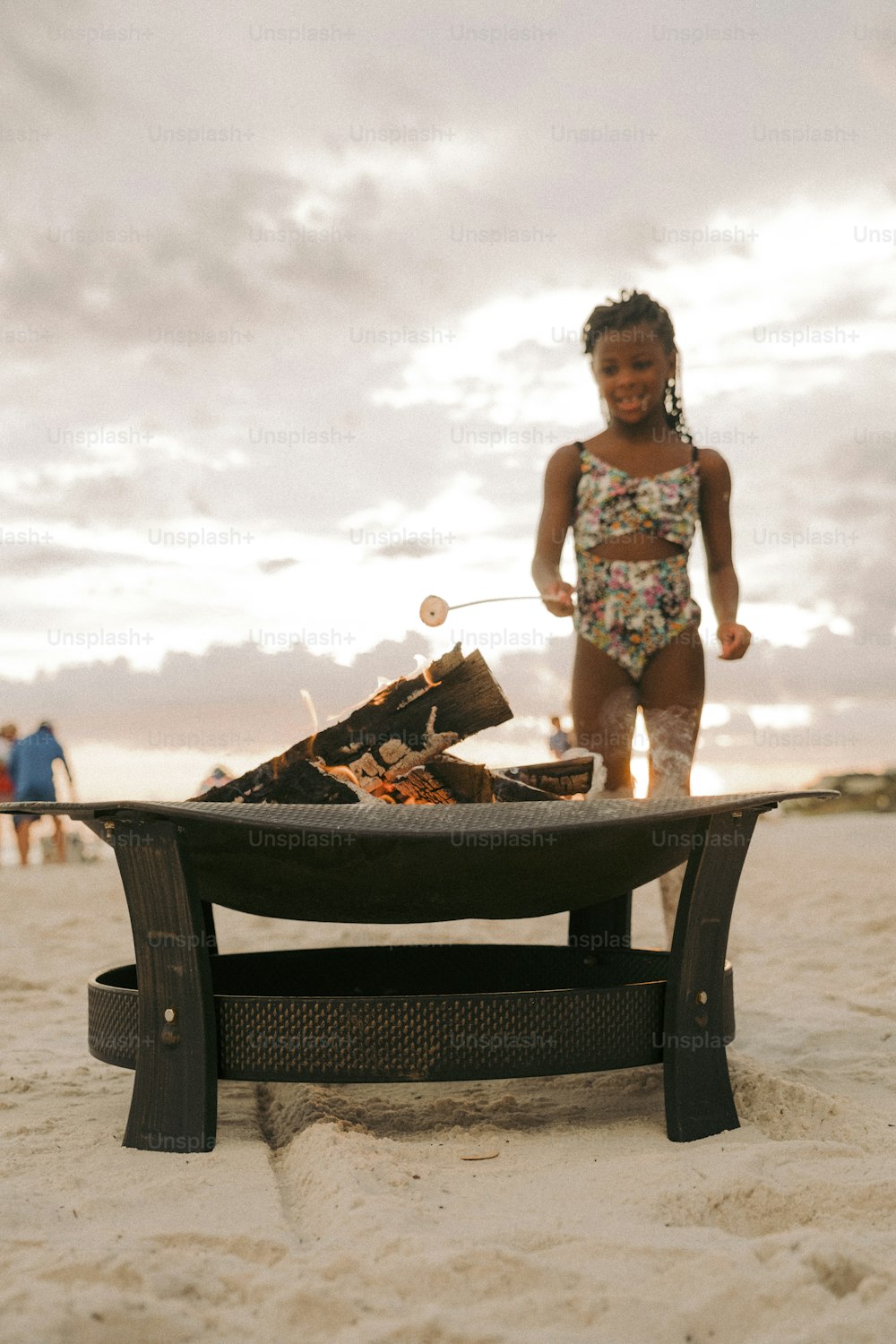 a little girl standing on a beach next to a grill