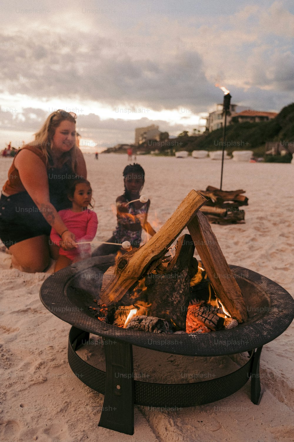 a woman kneeling down next to a fire pit on a beach