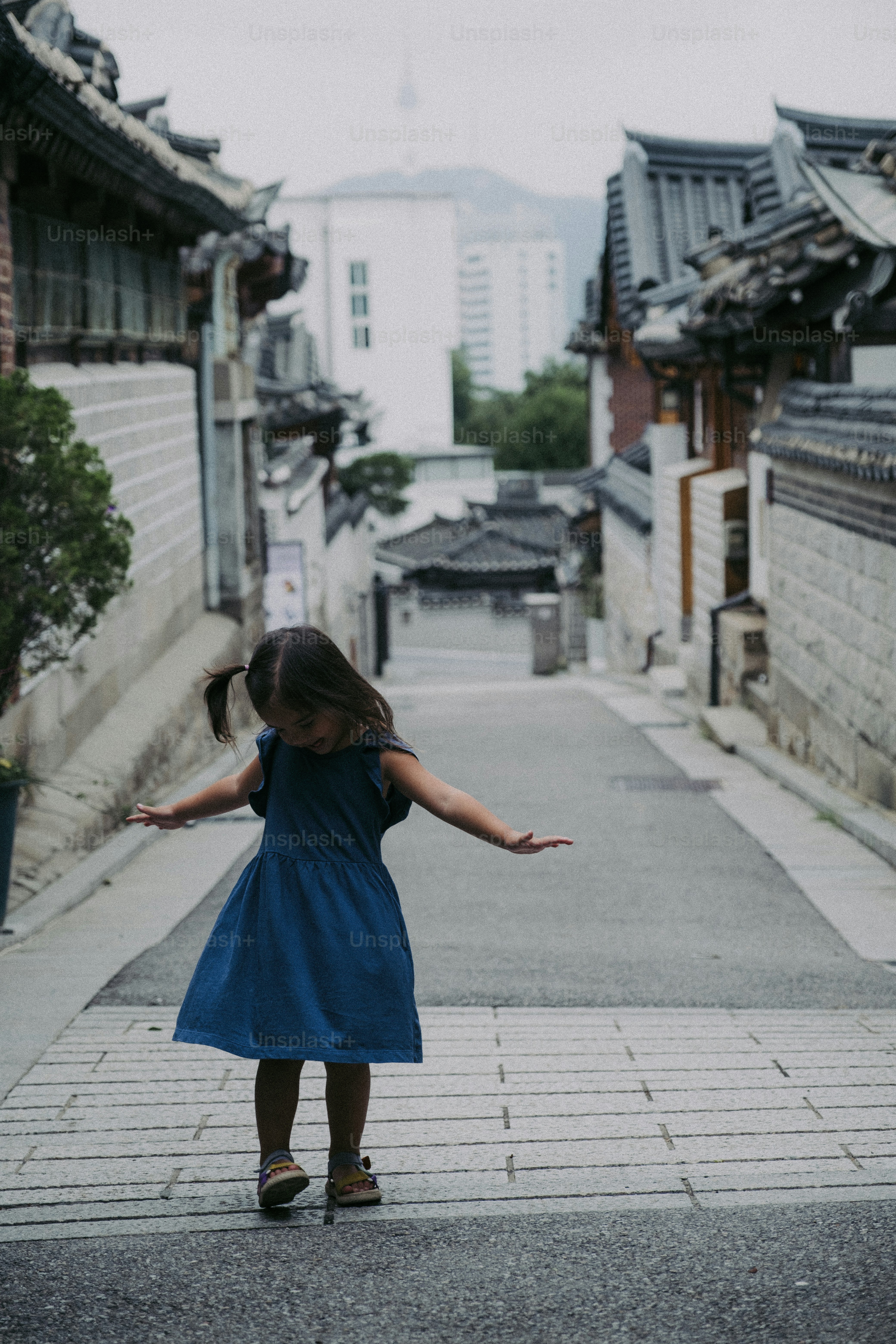 A little girl in a blue dress standing on a sidewalk photo – Brown hair ...