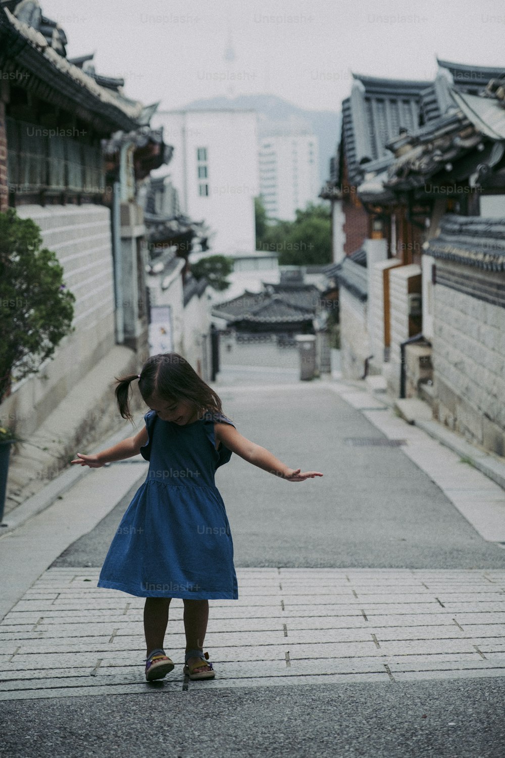 a little girl in a blue dress standing on a sidewalk