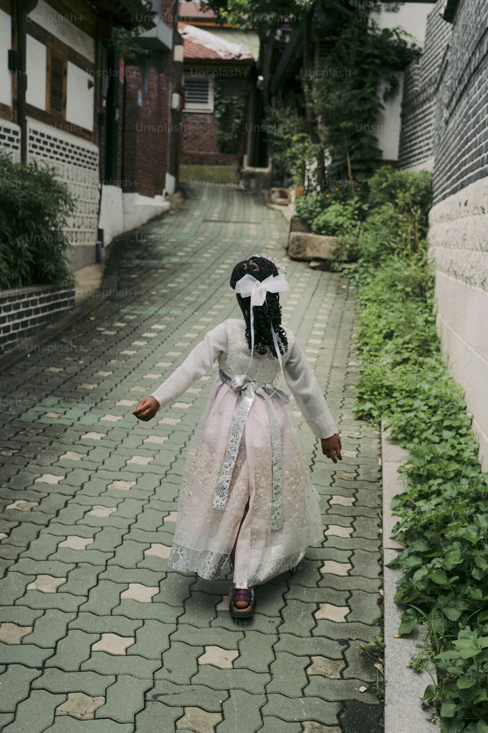uma menina em um vestido branco andando por uma rua