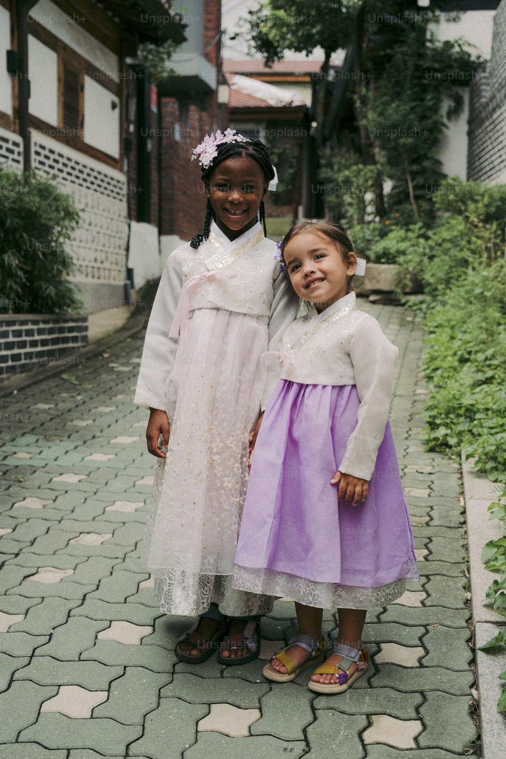 two little girls standing next to each other on a sidewalk