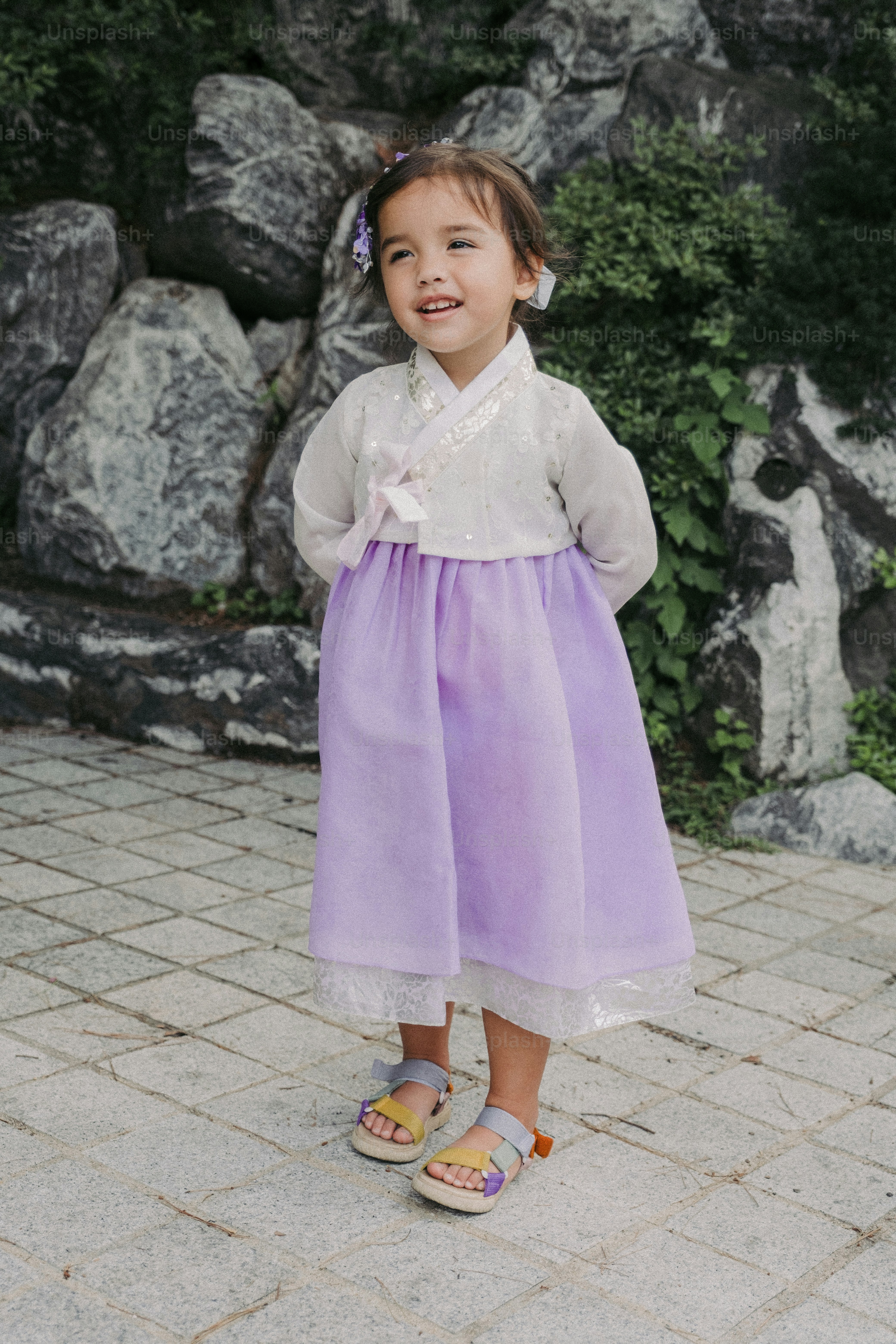 uma menina em um vestido roxo em pé na frente de algumas pedras