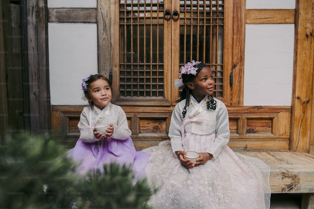 two young girls sitting on a bench in front of a building