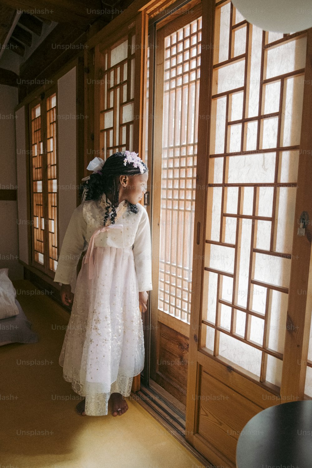a little girl in a white dress looking out a window