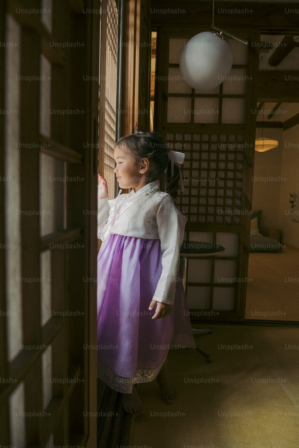a little girl in a purple and white dress looking out a window