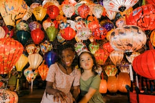 a couple of girls sitting next to each other in front of a wall of lanterns