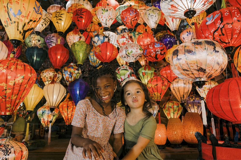 a couple of girls sitting next to each other in front of a wall of lanterns