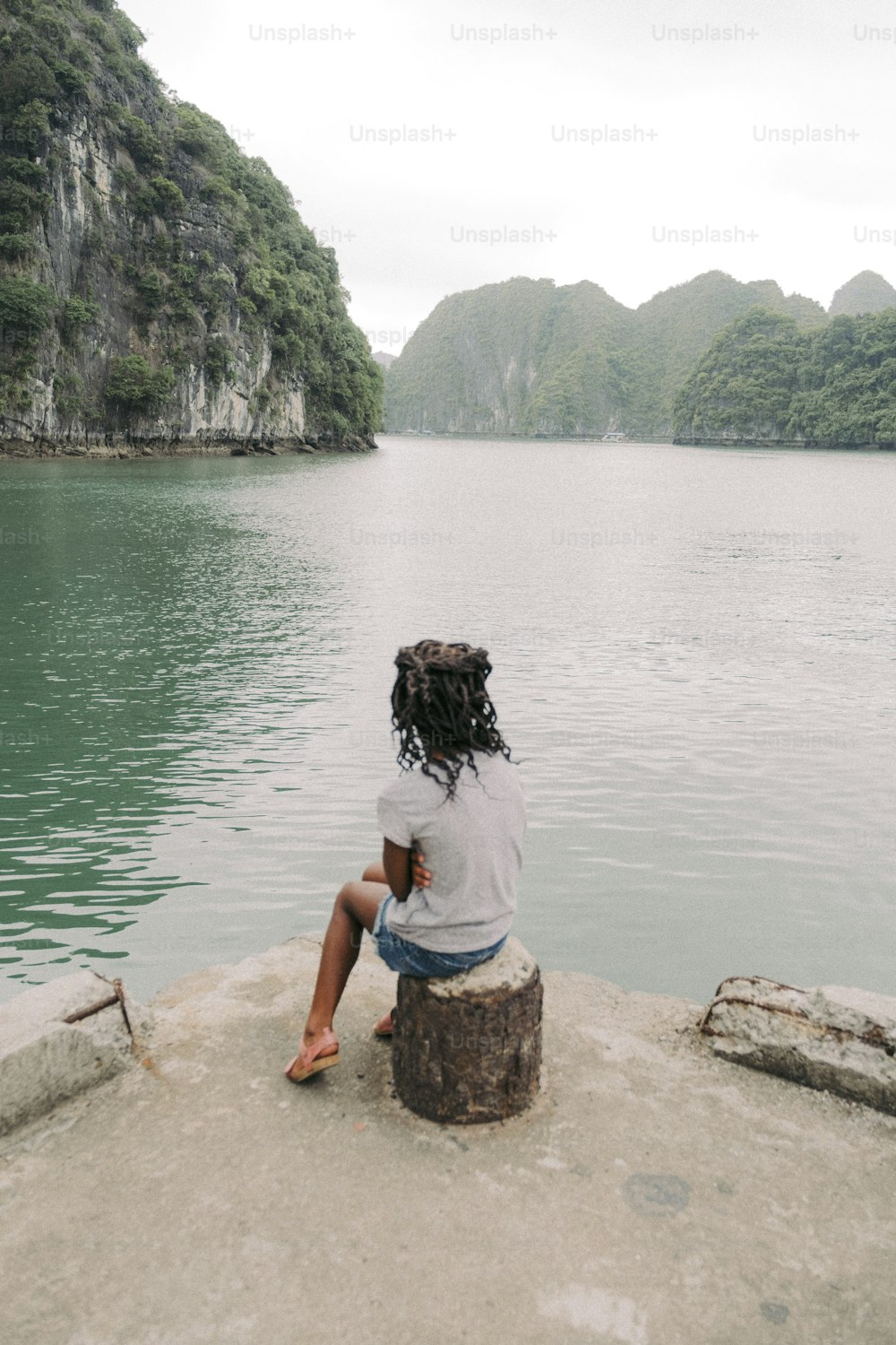 Una persona sentada en una roca cerca de un cuerpo de agua