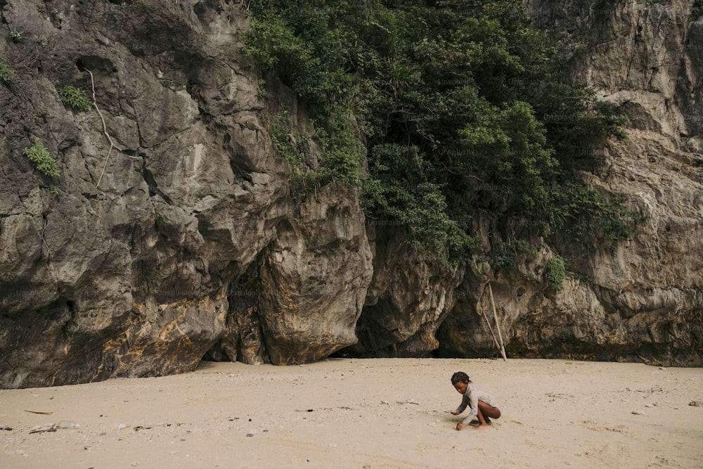 a person kneeling on a beach next to a cliff
