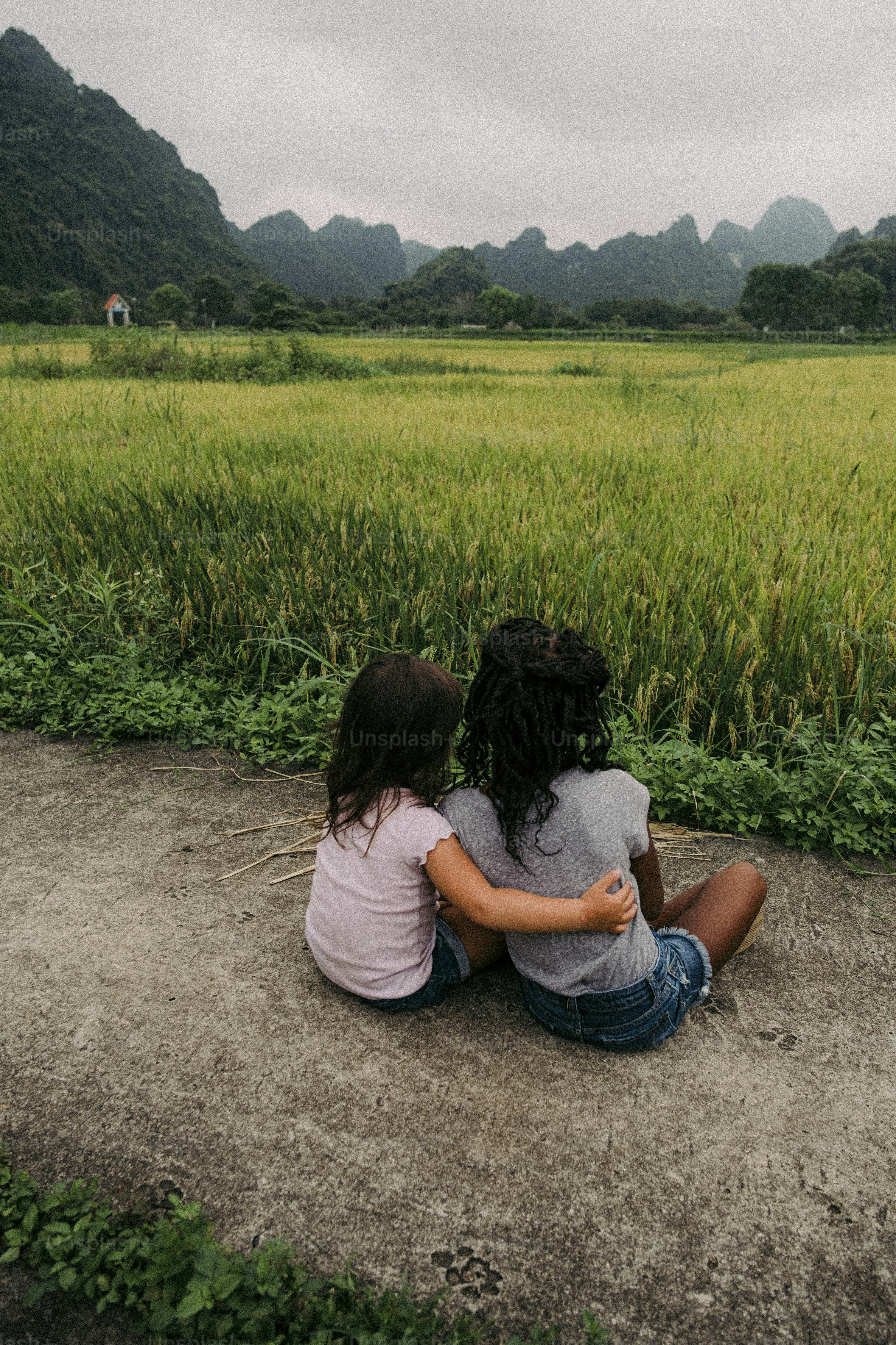 Two girls sitting on the ground in front of a field photo – Holiday ...