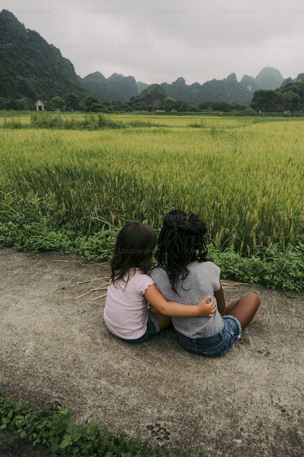 two girls sitting on the ground in front of a field