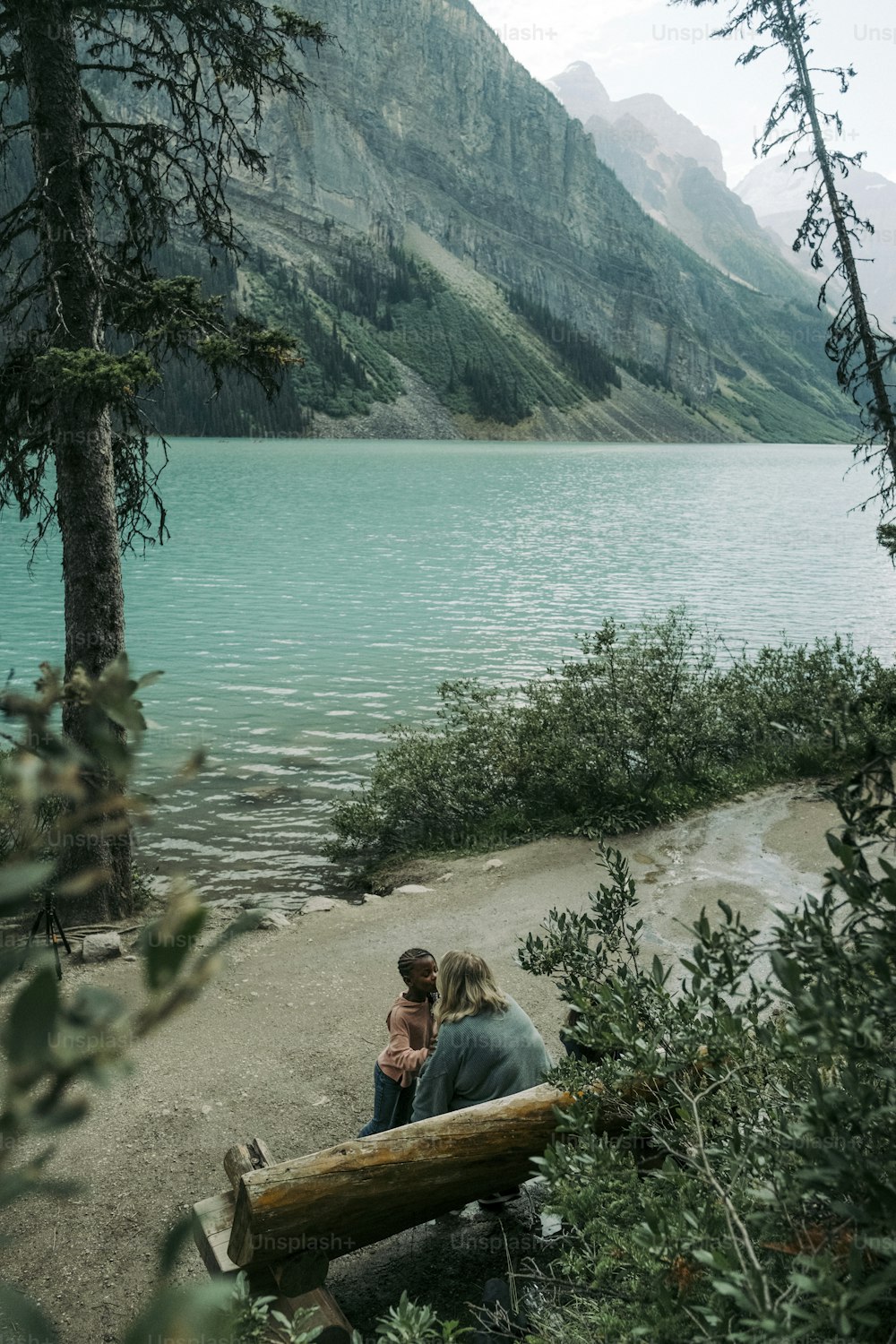 a man and woman sitting on a bench next to a lake
