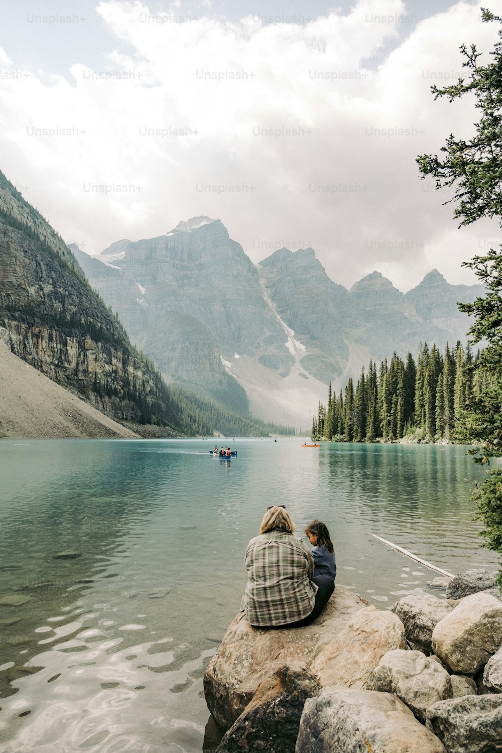 two people sitting on a rock near a lake