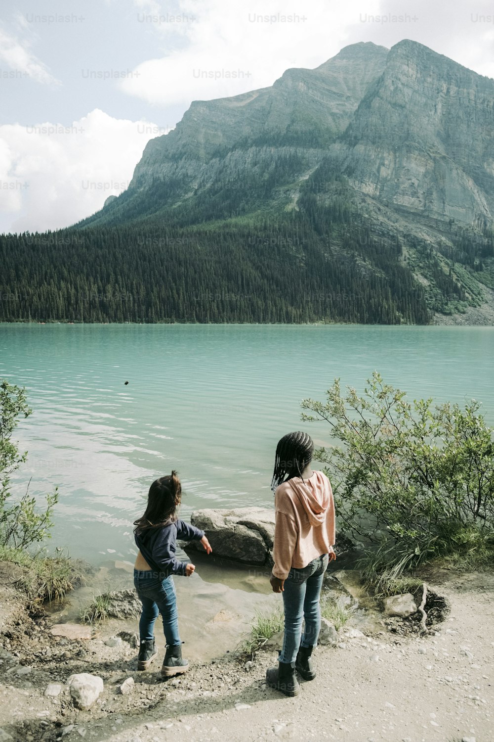 two young girls standing on the shore of a lake