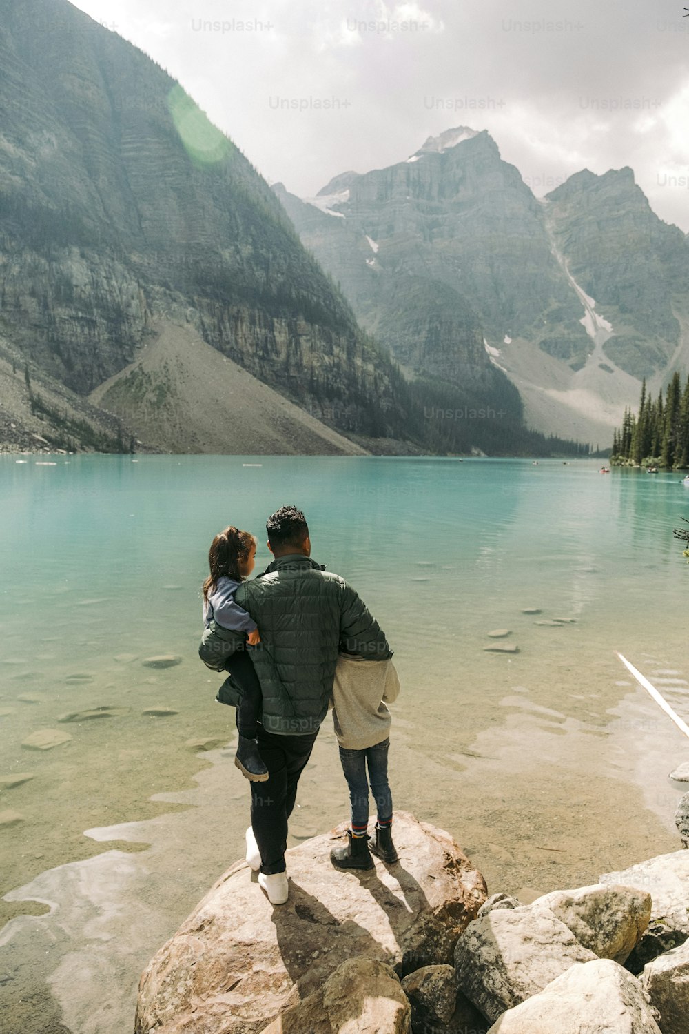 a man and a woman standing on a rock near a lake