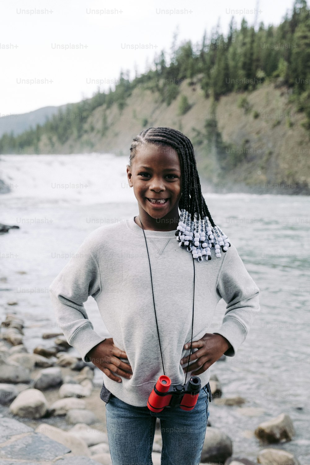 a young girl standing on a rocky beach next to a body of water