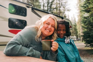 a woman holding a cup next to a girl in front of a camper