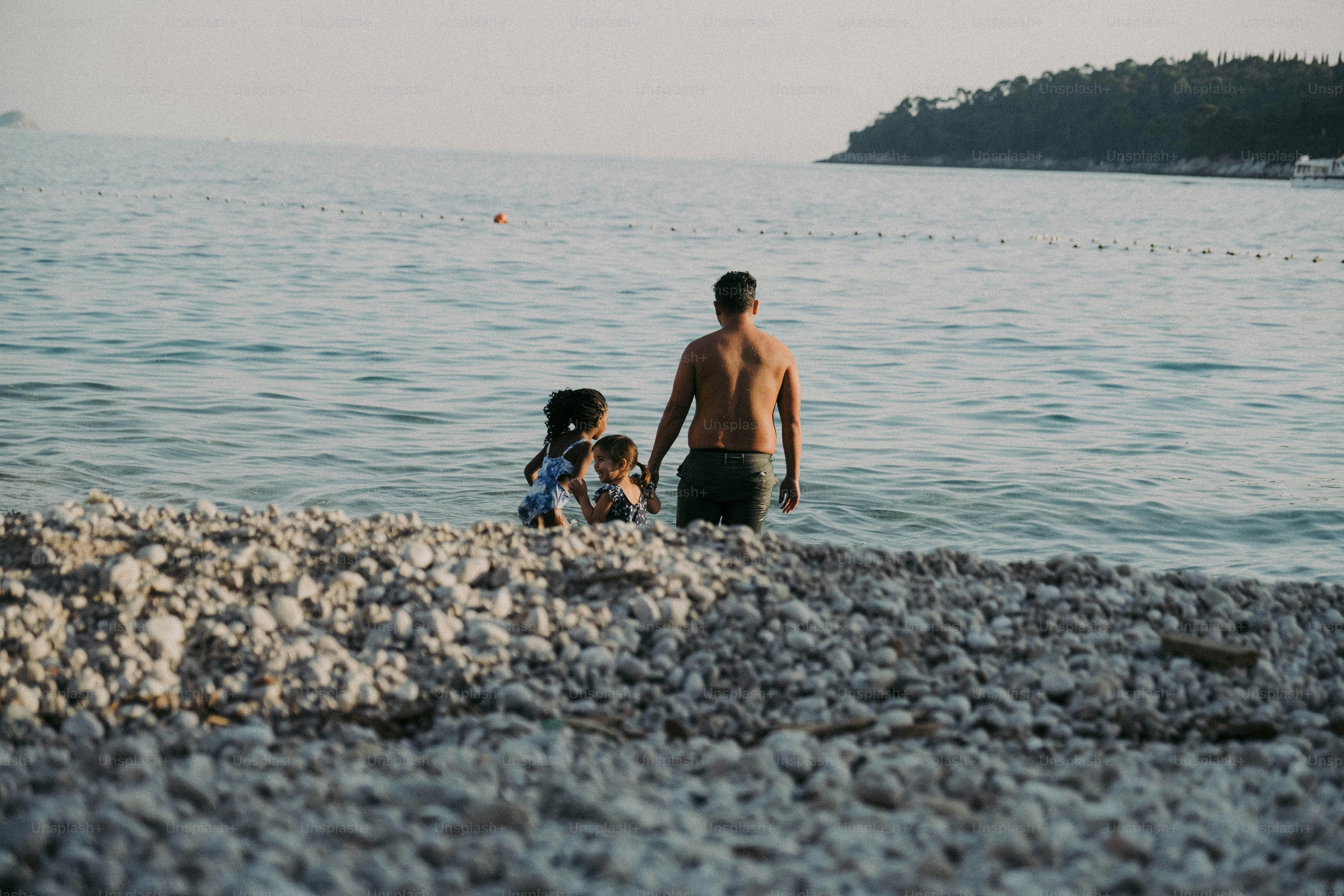 A man and a little girl standing on a beach next to a body of water ...