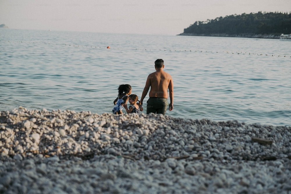 a man and a little girl standing on a beach next to a body of water