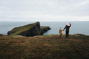 a man holding a child's backpack while standing on top of a hill