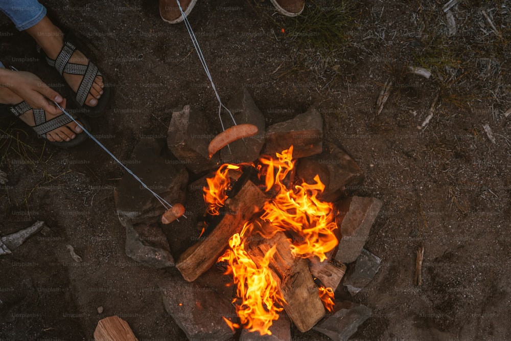 a person standing over a fire with hot dogs on it