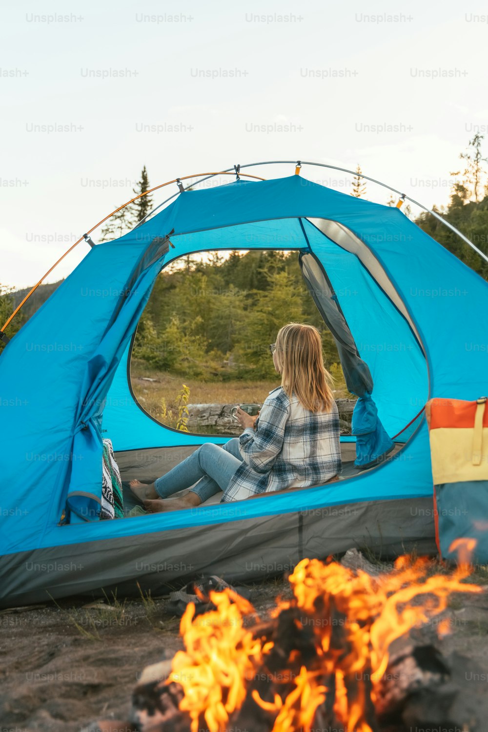 a woman sitting in a blue tent next to a fire
