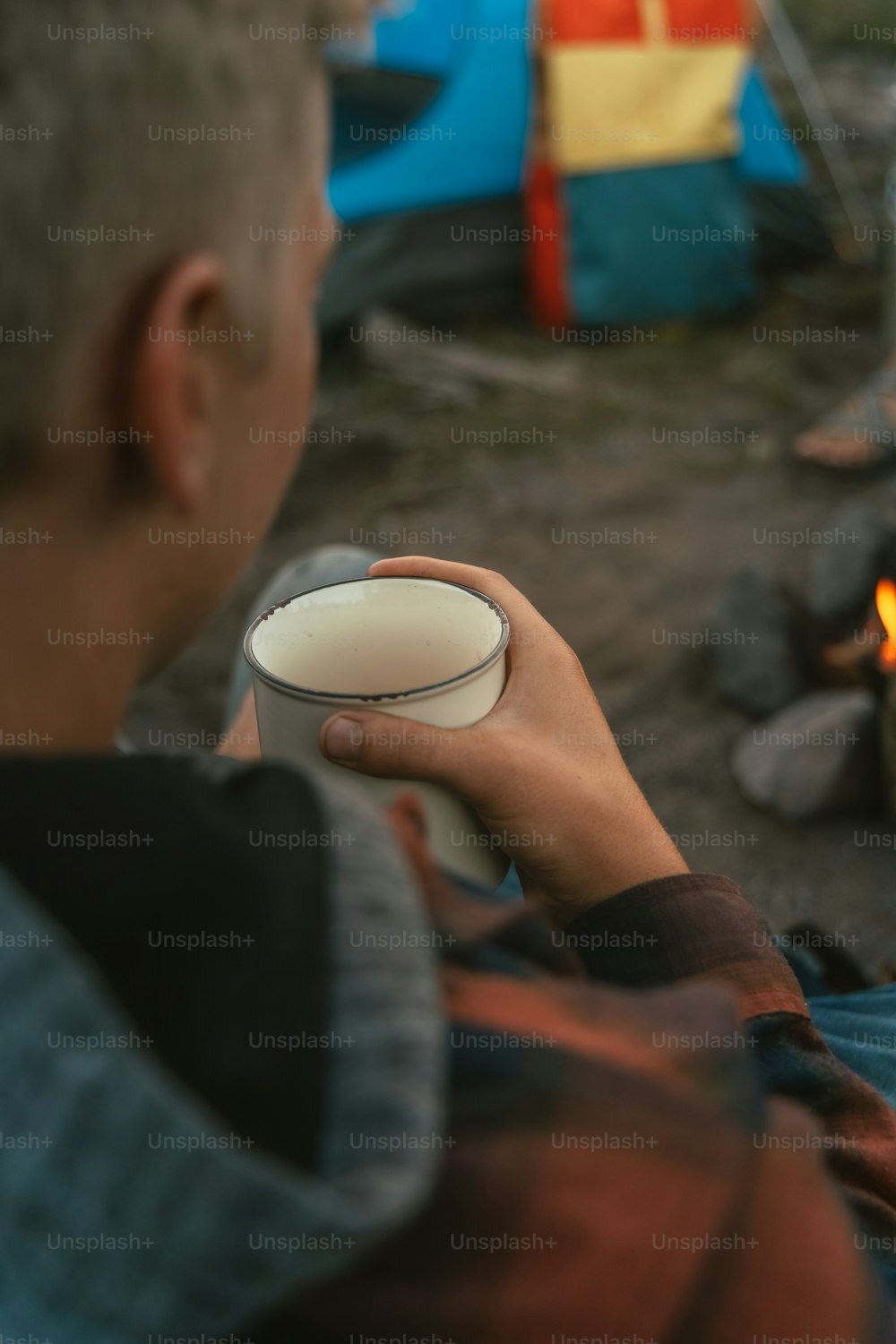 a man holding a white bowl near a campfire