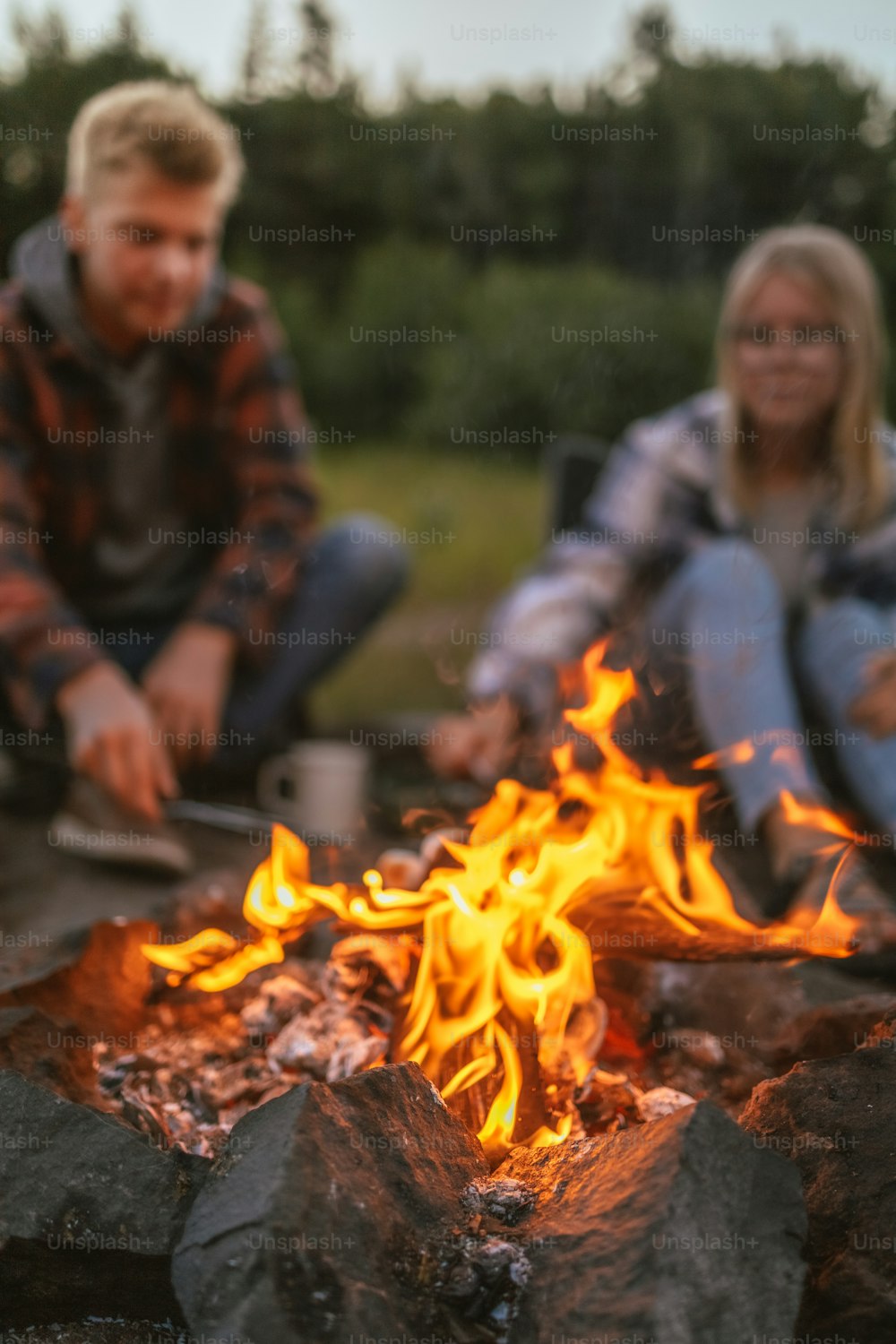 a man and a woman sitting next to a campfire
