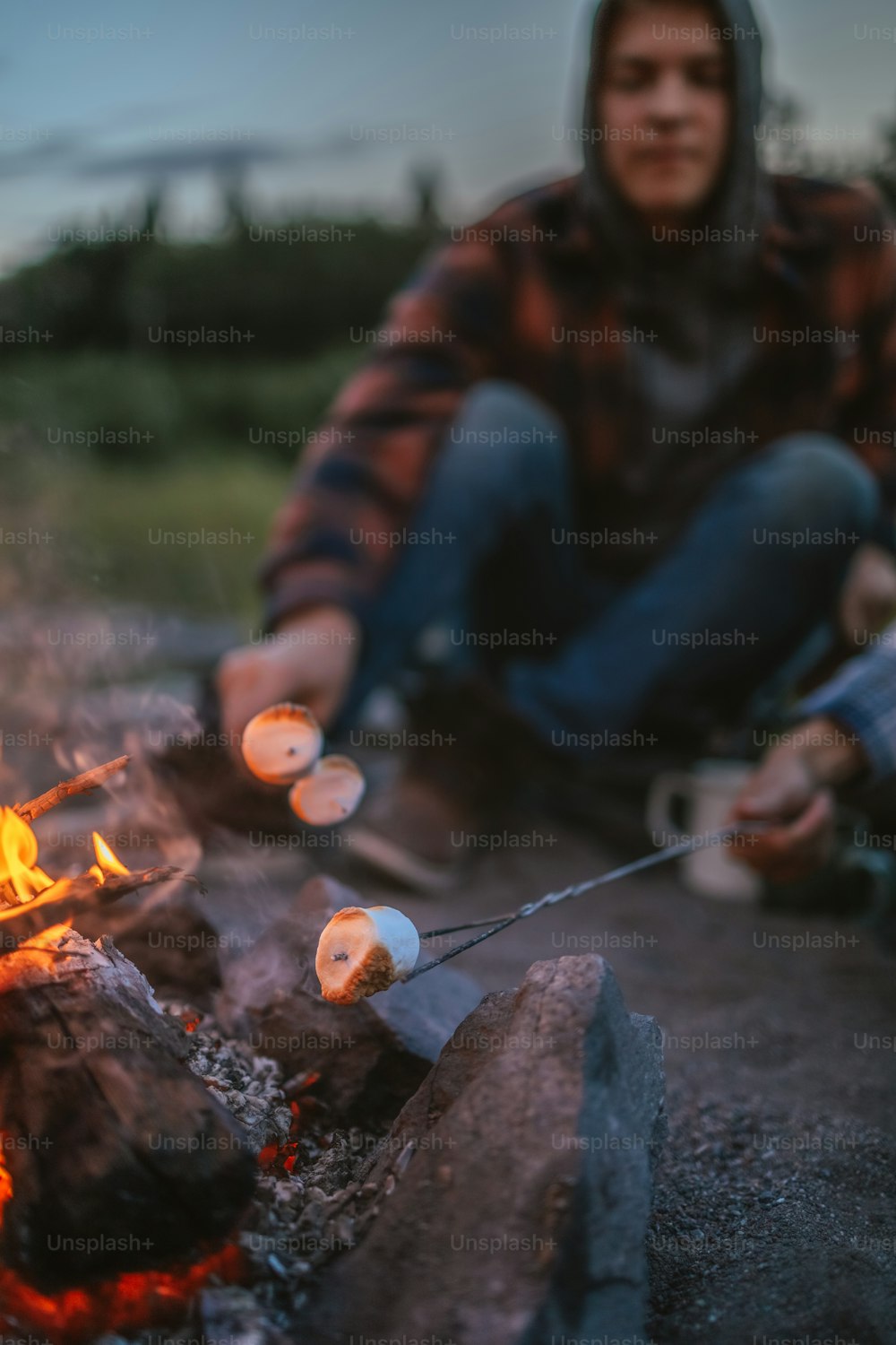 a man sitting in front of a campfire cooking marshmallows