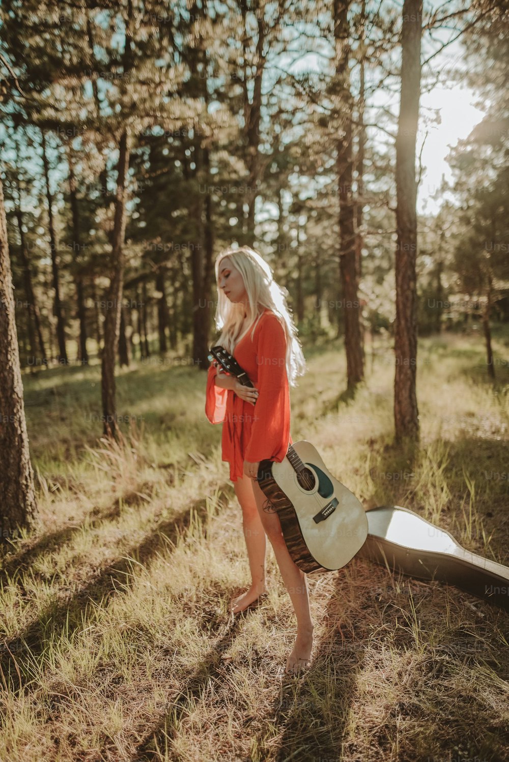 a woman standing in the woods holding a guitar