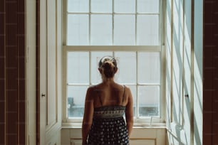 a woman standing in front of a window looking out