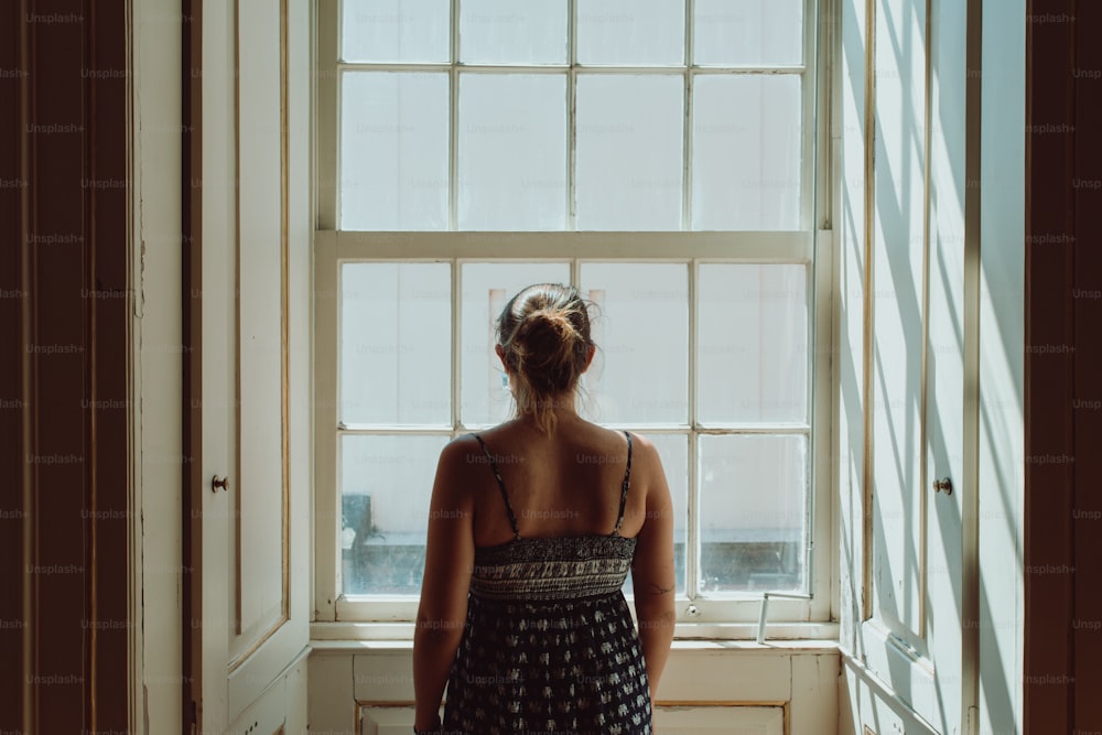 a woman standing in front of a window looking out