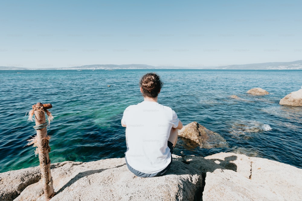 um homem sentado em uma rocha olhando para o oceano