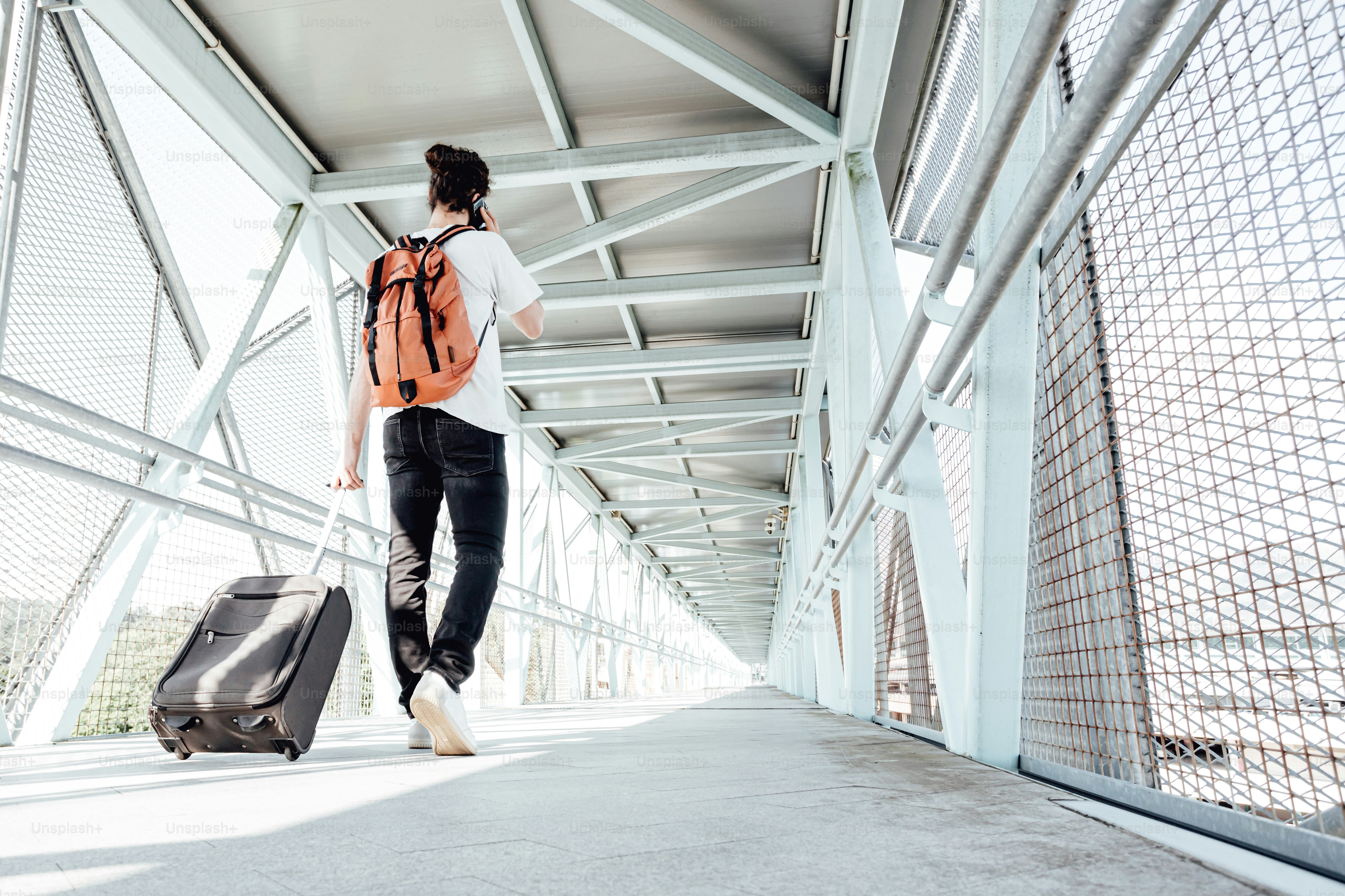 a woman with a backpack and suitcase walking across a bridge