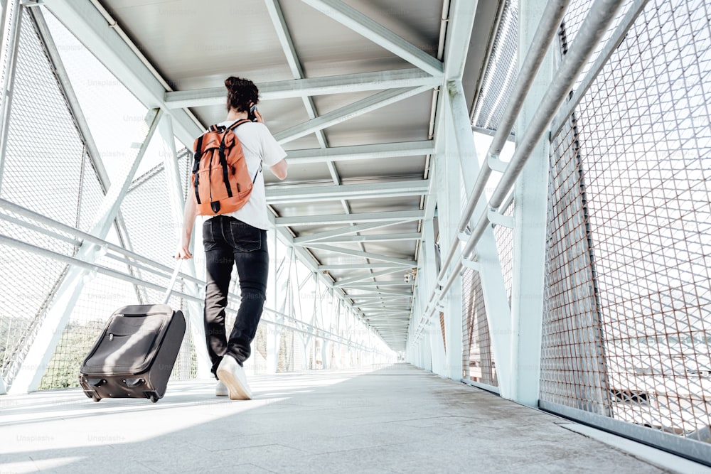 a woman with a backpack and suitcase walking across a bridge