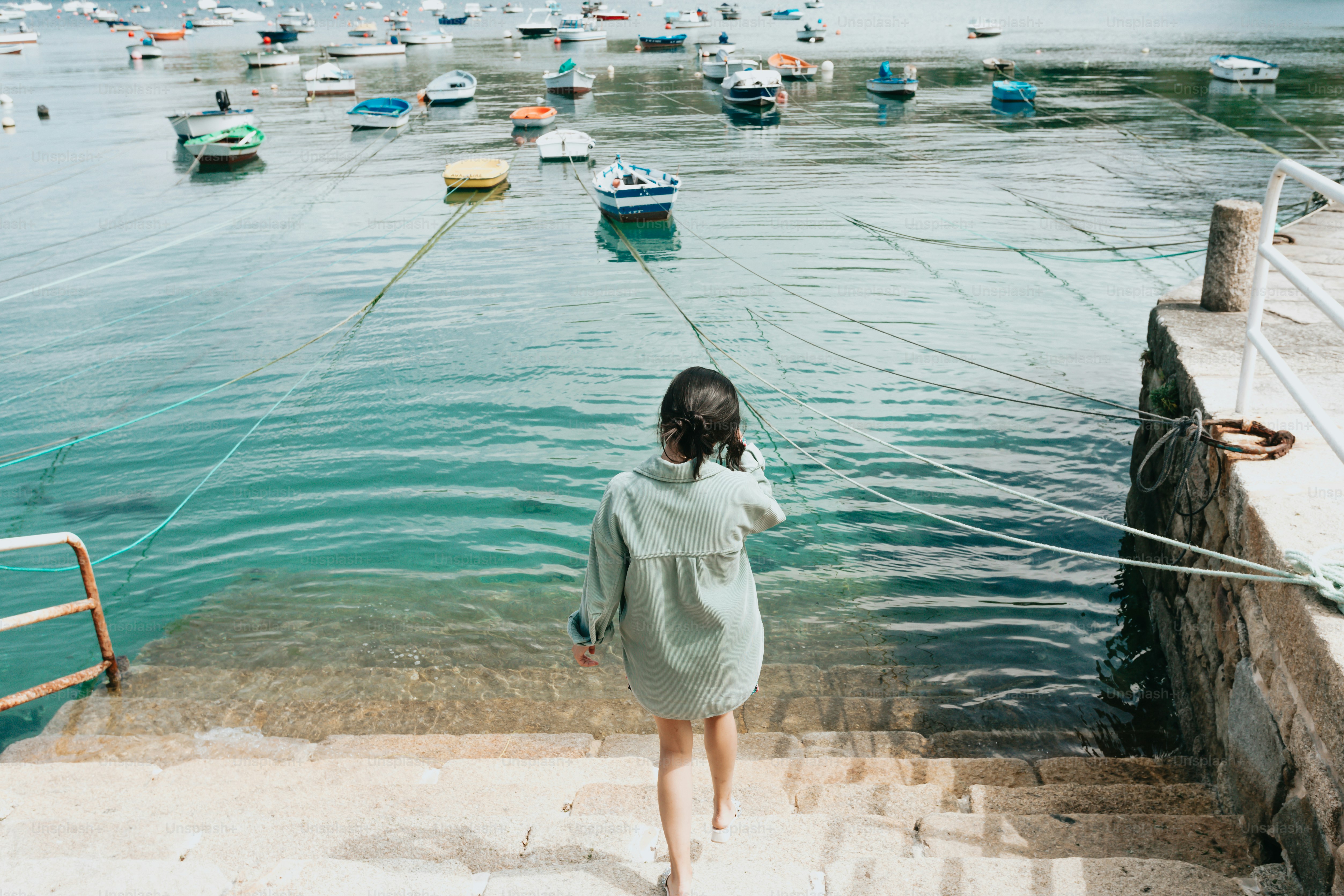 a woman walking up a flight of stairs towards a harbor filled with boats