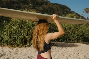 Una mujer sosteniendo una tabla de surf encima de su cabeza